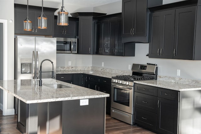 kitchen with sink, hanging light fixtures, a center island with sink, appliances with stainless steel finishes, and dark hardwood / wood-style floors