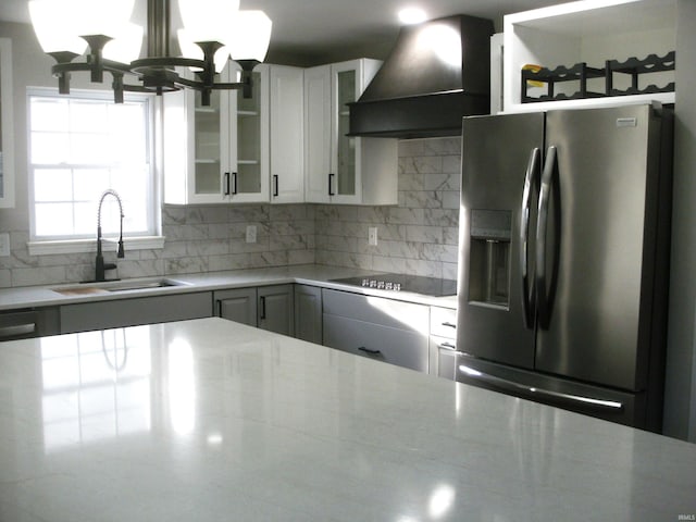 kitchen with sink, white cabinetry, stainless steel fridge, custom range hood, and black electric stovetop