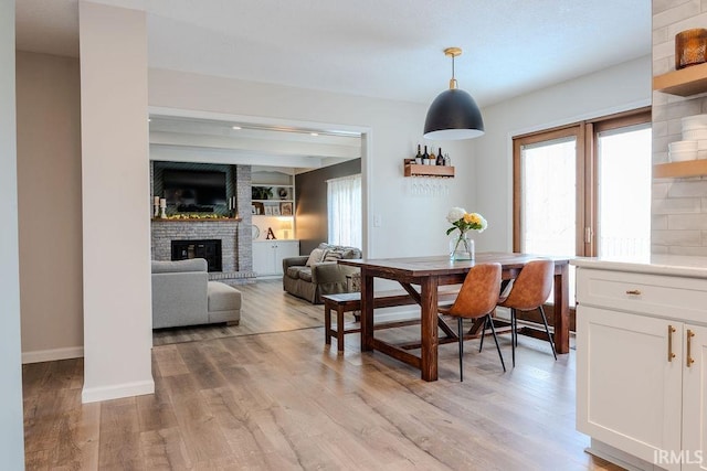 dining room featuring a brick fireplace, built in shelves, and light hardwood / wood-style floors