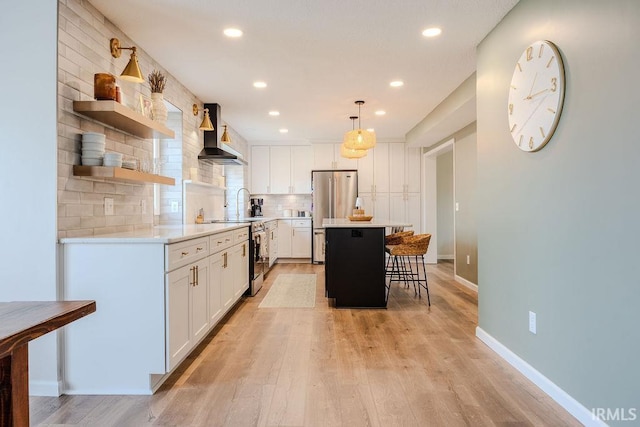 kitchen featuring pendant lighting, wall chimney range hood, appliances with stainless steel finishes, white cabinetry, and a center island