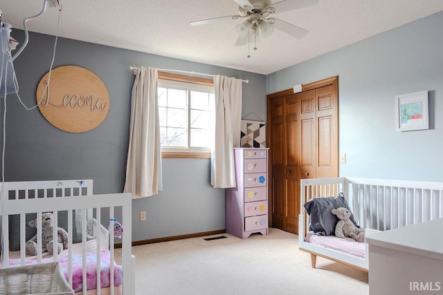 carpeted bedroom featuring a nursery area, ceiling fan, and a closet