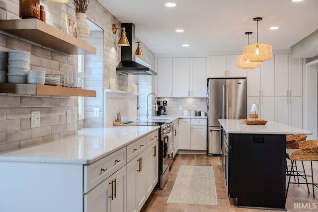 kitchen with pendant lighting, wall chimney range hood, appliances with stainless steel finishes, white cabinetry, and backsplash