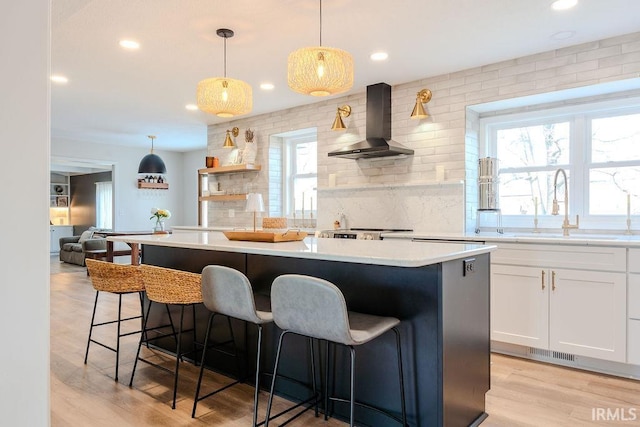 kitchen with a breakfast bar area, a center island, white cabinets, decorative light fixtures, and wall chimney exhaust hood