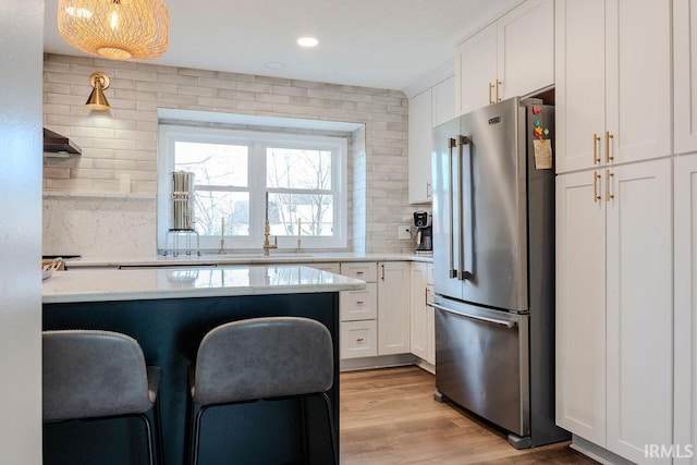 kitchen featuring a breakfast bar, high end fridge, light hardwood / wood-style flooring, pendant lighting, and white cabinets