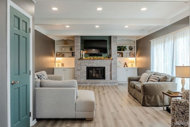 living room with beamed ceiling, a brick fireplace, light hardwood / wood-style floors, and built in shelves