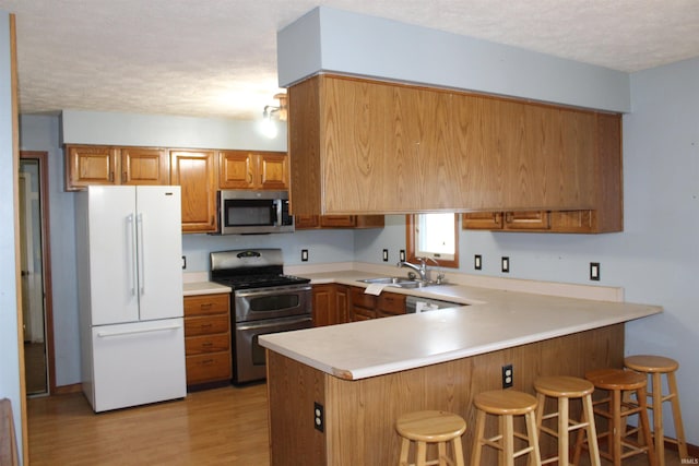 kitchen with a breakfast bar area, kitchen peninsula, stainless steel appliances, a textured ceiling, and light hardwood / wood-style flooring