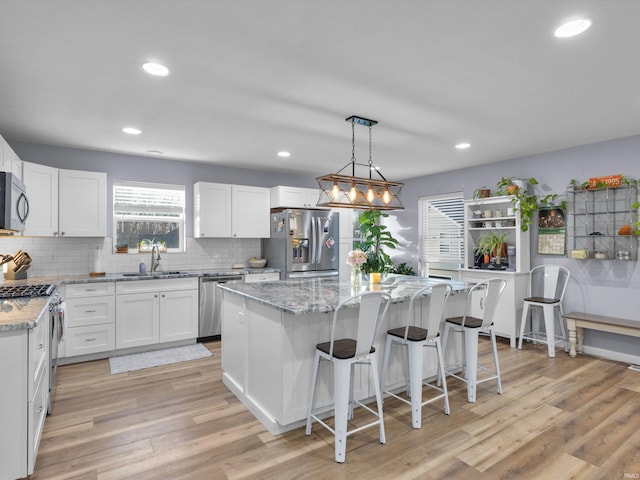 kitchen featuring appliances with stainless steel finishes, white cabinetry, sink, a center island, and light stone countertops