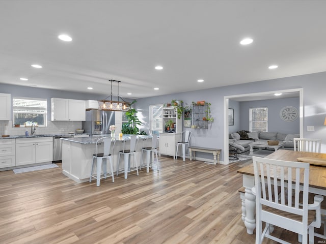 kitchen with a kitchen island, appliances with stainless steel finishes, white cabinets, a kitchen breakfast bar, and hanging light fixtures