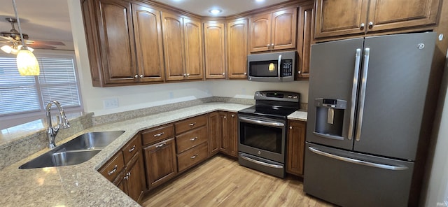 kitchen with pendant lighting, sink, appliances with stainless steel finishes, light stone counters, and light wood-type flooring