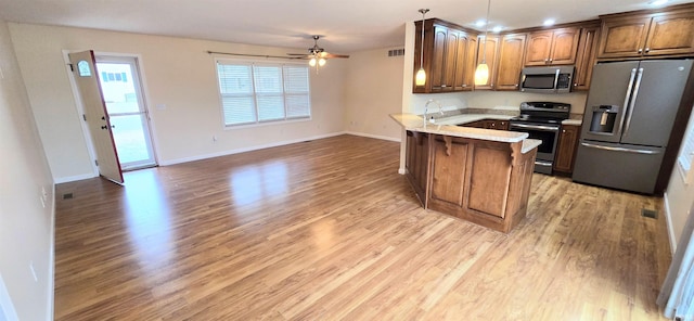 kitchen featuring hanging light fixtures, ceiling fan, kitchen peninsula, stainless steel appliances, and light hardwood / wood-style flooring