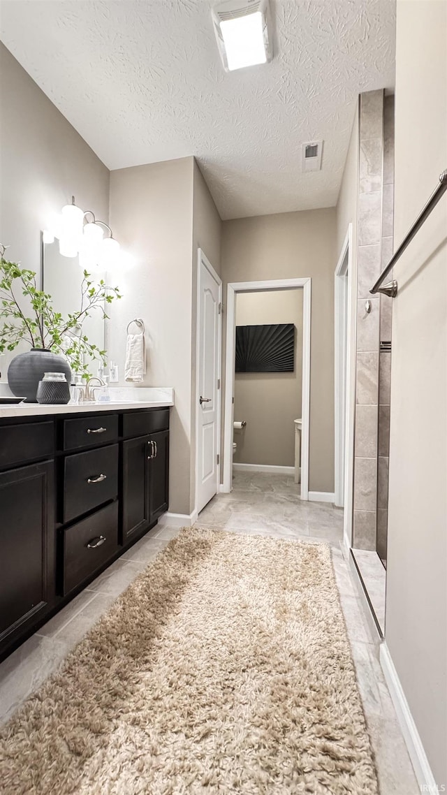 bathroom with a tile shower, vanity, and a textured ceiling