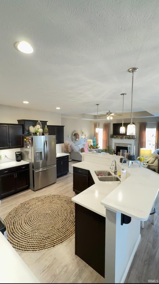 kitchen with sink, hanging light fixtures, a center island with sink, stainless steel fridge with ice dispenser, and light wood-type flooring