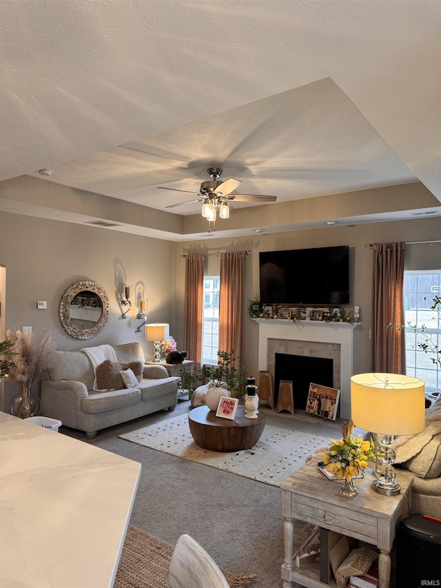 carpeted living room featuring ceiling fan, a fireplace, a raised ceiling, and a textured ceiling