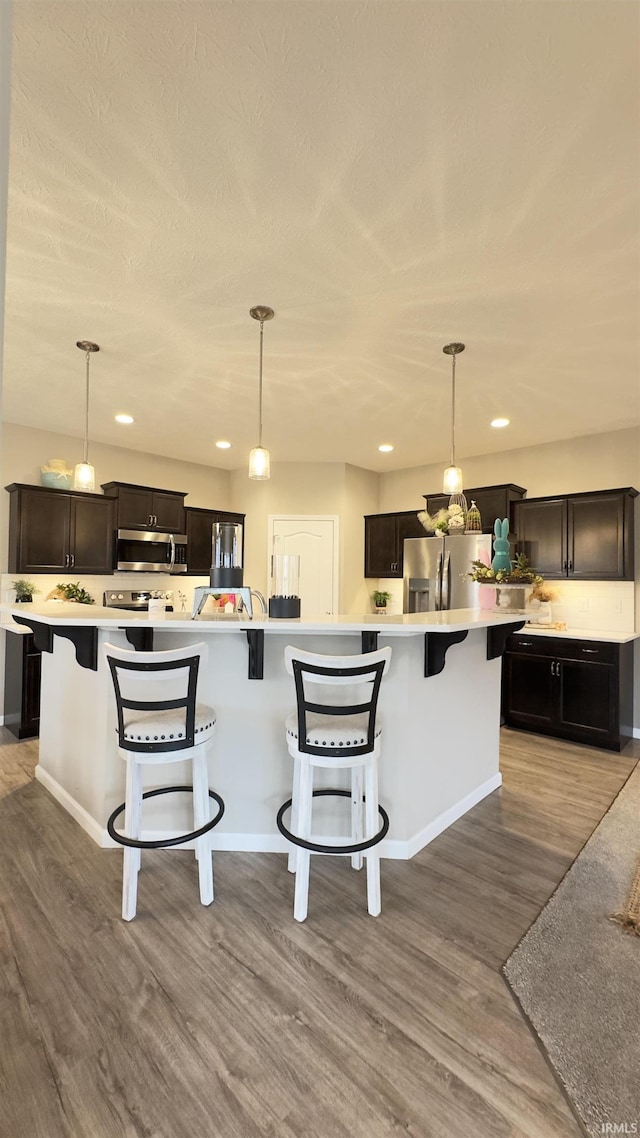 kitchen featuring decorative light fixtures, a breakfast bar, a large island with sink, and appliances with stainless steel finishes