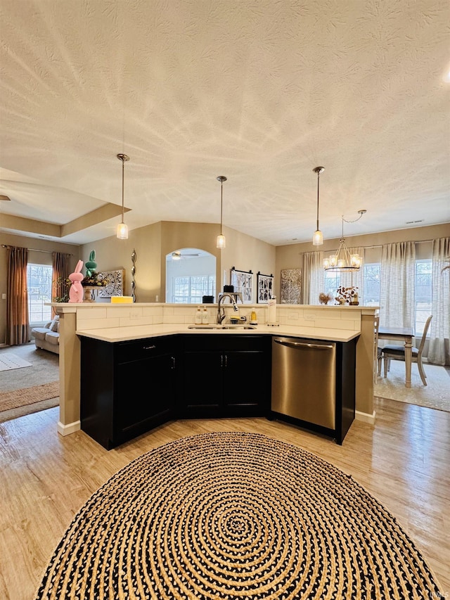 kitchen with sink, decorative light fixtures, dishwasher, and a kitchen island with sink