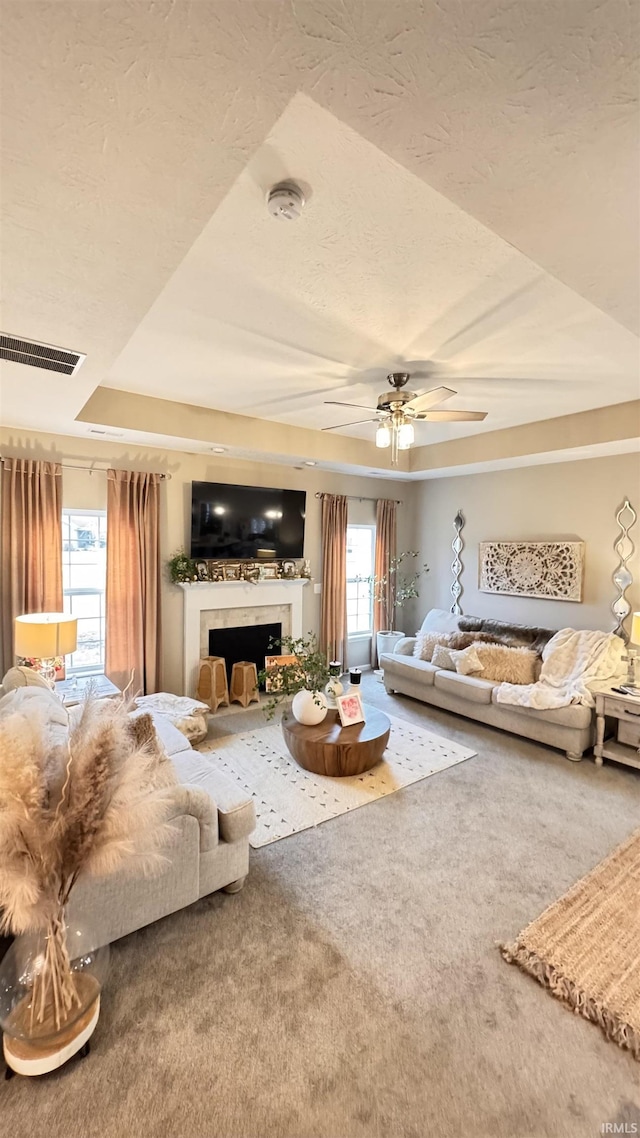 living room with a raised ceiling, ceiling fan, carpet floors, and a textured ceiling