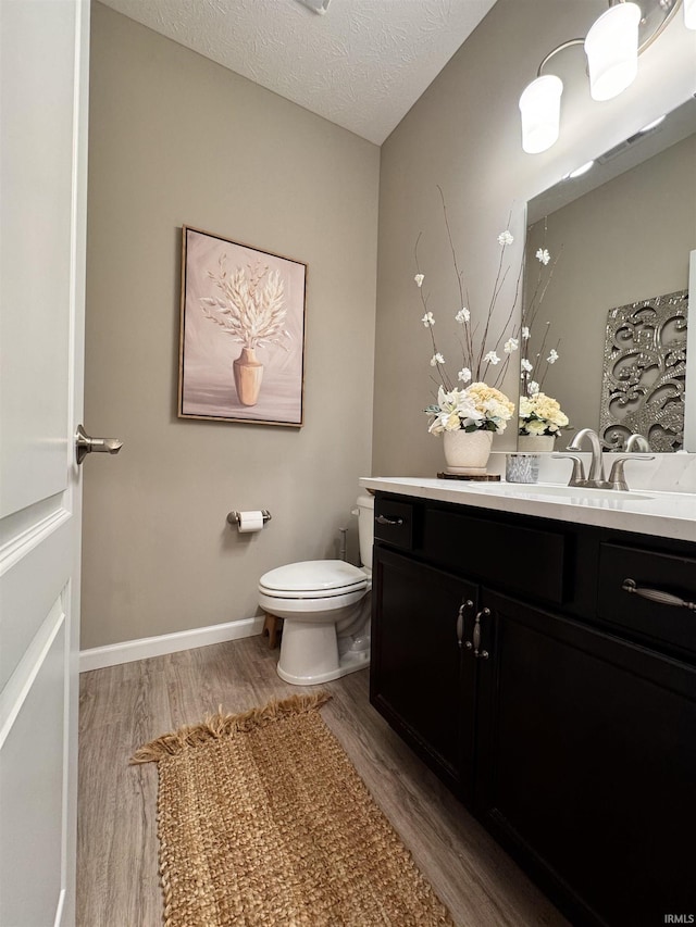 bathroom featuring wood-type flooring, toilet, a textured ceiling, and vanity