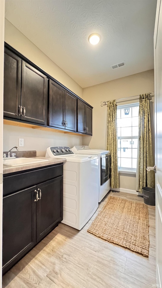 clothes washing area featuring cabinets, separate washer and dryer, and light wood-type flooring