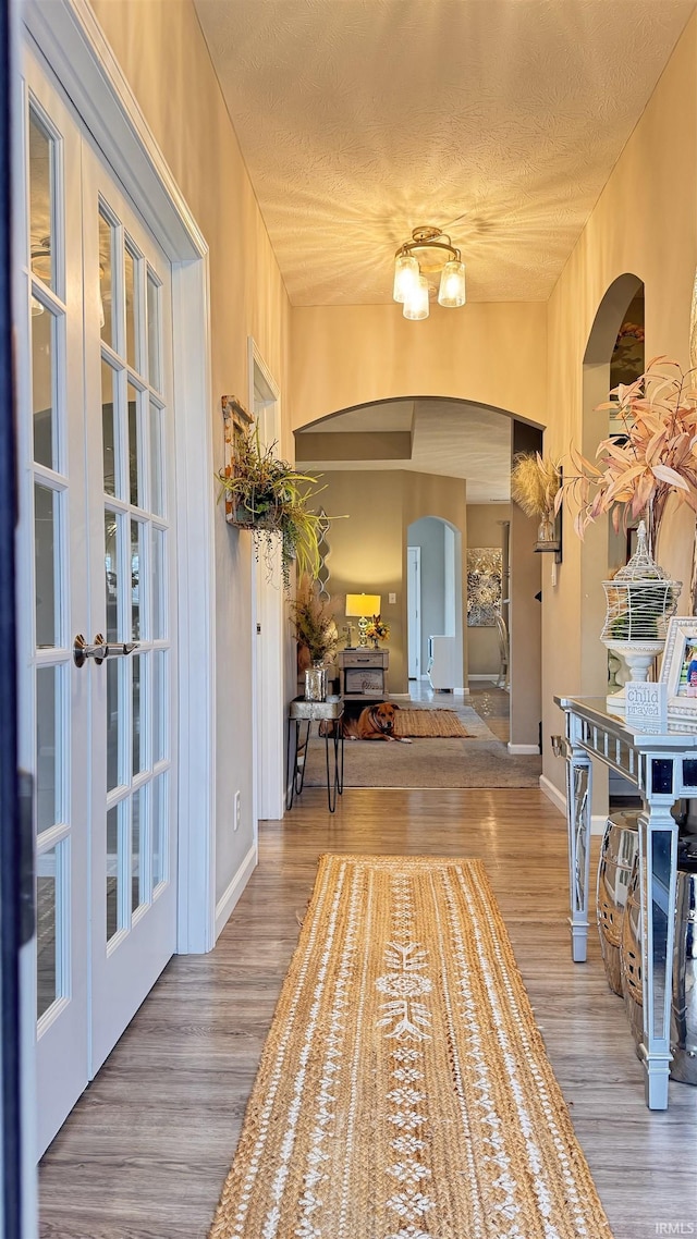 hallway with light hardwood / wood-style floors, french doors, and a textured ceiling