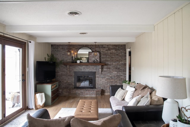 living room featuring a brick fireplace, light wood-type flooring, a textured ceiling, and beam ceiling