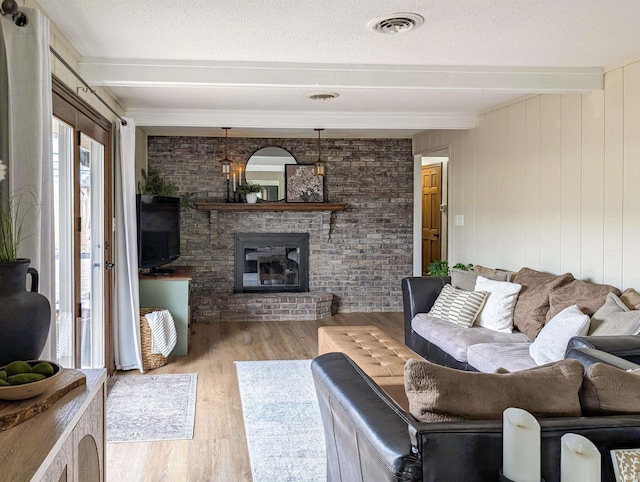 living room with beamed ceiling, a brick fireplace, light hardwood / wood-style flooring, and a textured ceiling