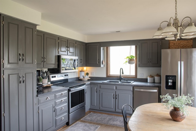 kitchen with stainless steel appliances, sink, gray cabinetry, and a notable chandelier