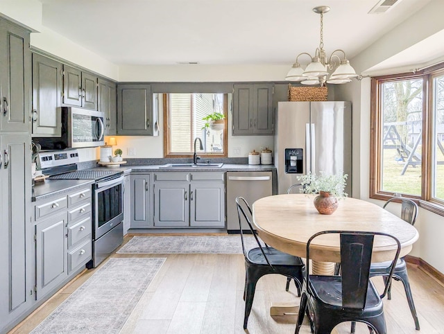 kitchen featuring pendant lighting, sink, light hardwood / wood-style flooring, appliances with stainless steel finishes, and an inviting chandelier