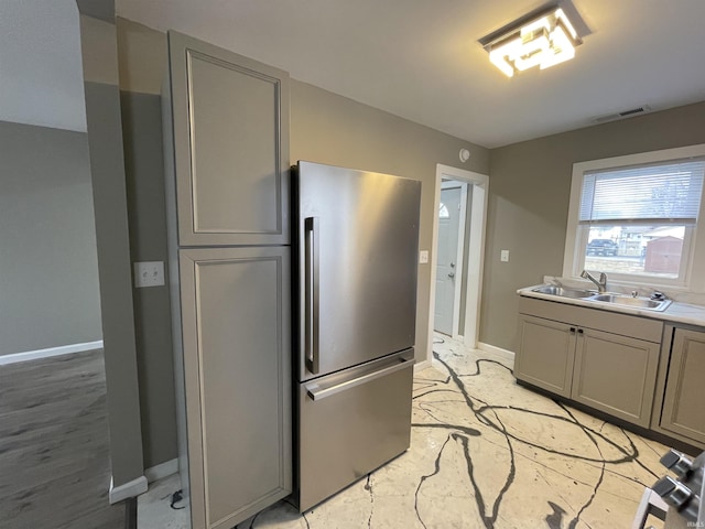 kitchen with gray cabinetry, sink, and stainless steel refrigerator