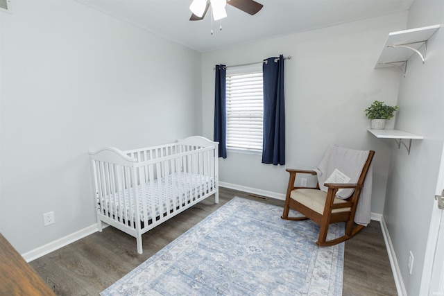 bedroom featuring a crib, ceiling fan, and dark hardwood / wood-style flooring