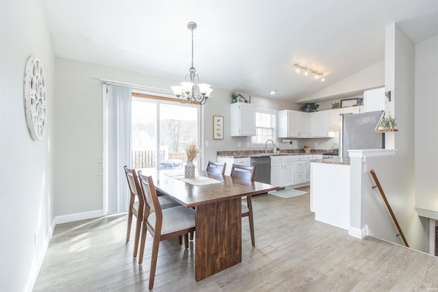 dining room featuring sink, vaulted ceiling, a chandelier, and light wood-type flooring