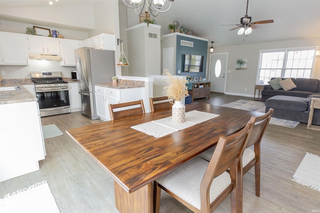 dining space featuring sink, ceiling fan with notable chandelier, high vaulted ceiling, and light wood-type flooring