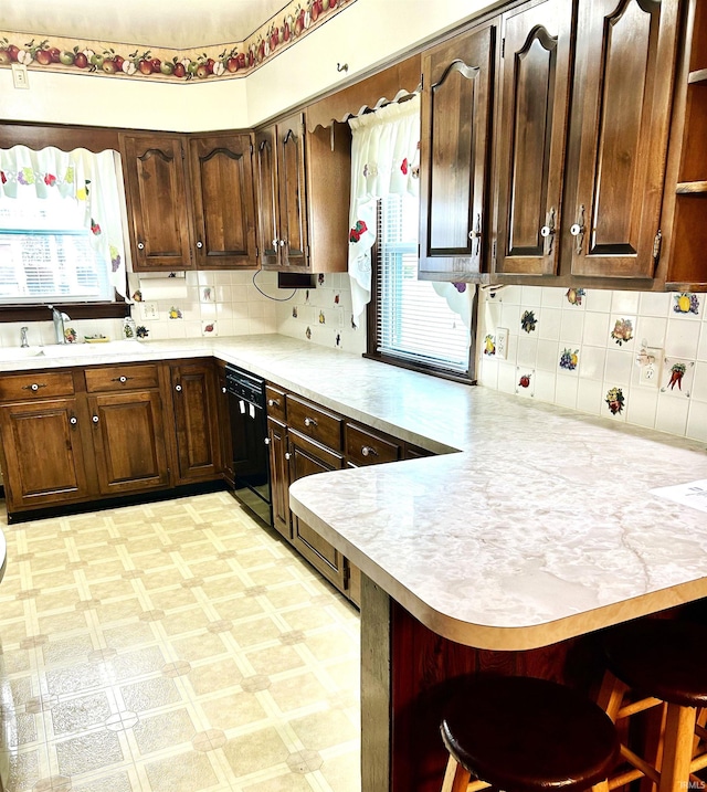 kitchen featuring decorative backsplash, a breakfast bar area, kitchen peninsula, and black dishwasher