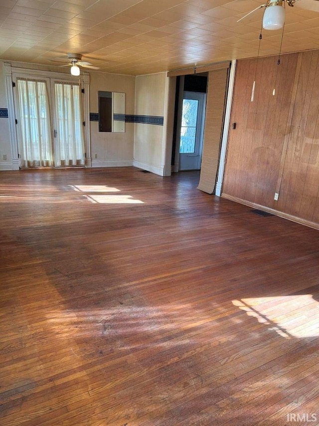 spare room with dark wood-type flooring, ceiling fan, and wooden walls