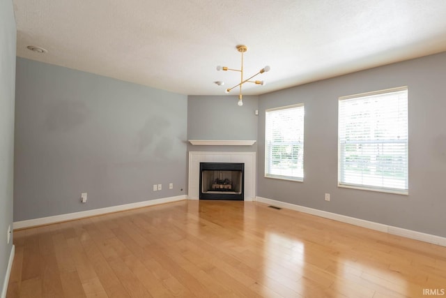 unfurnished living room featuring a fireplace, a chandelier, light hardwood / wood-style floors, and a textured ceiling