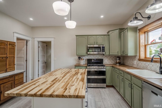 kitchen featuring butcher block counters, sink, green cabinetry, decorative light fixtures, and appliances with stainless steel finishes