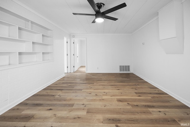 spare room with crown molding, built in features, ceiling fan, hardwood / wood-style floors, and brick wall