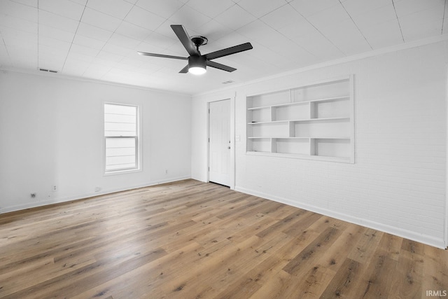 empty room with brick wall, wood-type flooring, built in features, and ornamental molding