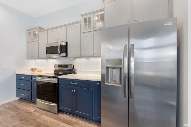 kitchen with stainless steel appliances, white cabinetry, blue cabinetry, and light hardwood / wood-style floors