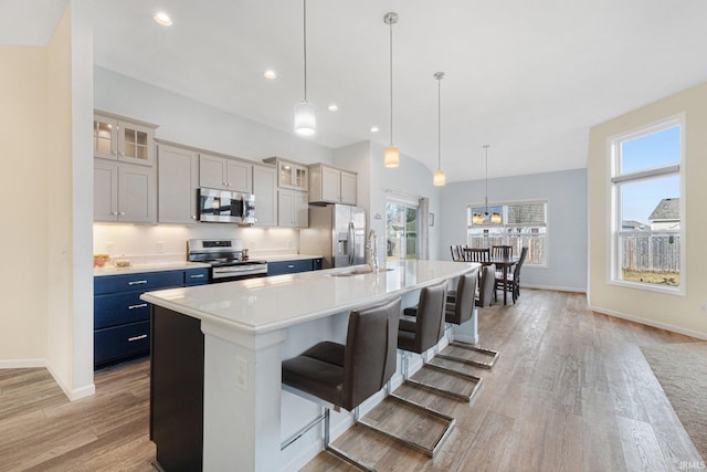 kitchen with a spacious island, a breakfast bar, gray cabinetry, decorative light fixtures, and appliances with stainless steel finishes