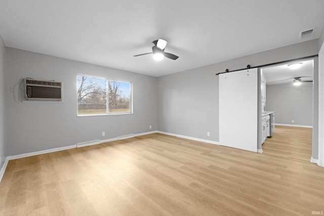 unfurnished bedroom featuring ceiling fan, a wall unit AC, a barn door, and light hardwood / wood-style flooring