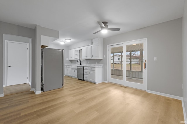 kitchen featuring appliances with stainless steel finishes, white cabinetry, sink, ceiling fan, and light hardwood / wood-style flooring