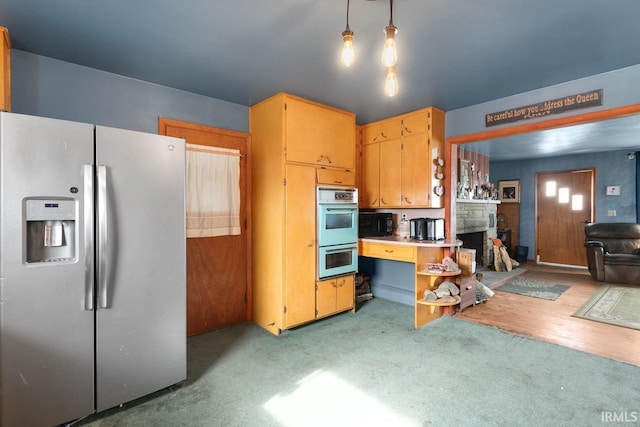 kitchen featuring stainless steel fridge, a stone fireplace, double oven, and hanging light fixtures