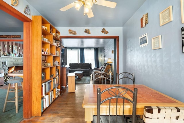 dining space with hardwood / wood-style floors, a fireplace, and ceiling fan