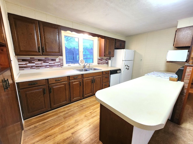 kitchen with tasteful backsplash, dishwasher, sink, white refrigerator, and light hardwood / wood-style flooring