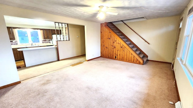 unfurnished living room with sink, light colored carpet, and ceiling fan