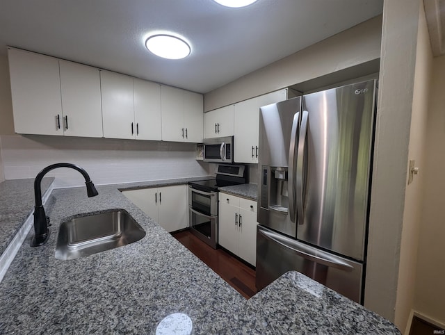 kitchen with appliances with stainless steel finishes, sink, dark stone countertops, and white cabinets