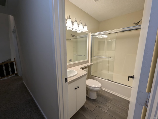 full bathroom featuring vanity, combined bath / shower with glass door, a textured ceiling, and toilet