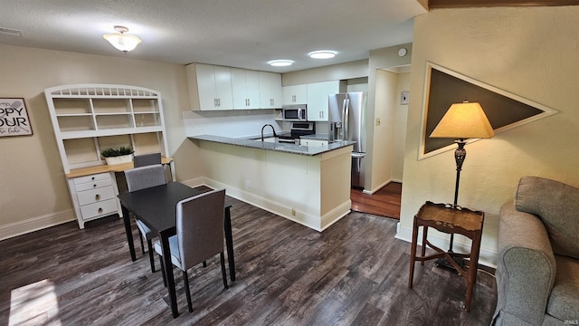 kitchen with dark hardwood / wood-style flooring, kitchen peninsula, white cabinets, and appliances with stainless steel finishes