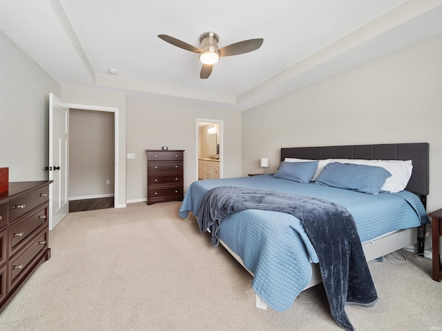 bedroom with a tray ceiling, light colored carpet, ceiling fan, and ensuite bathroom