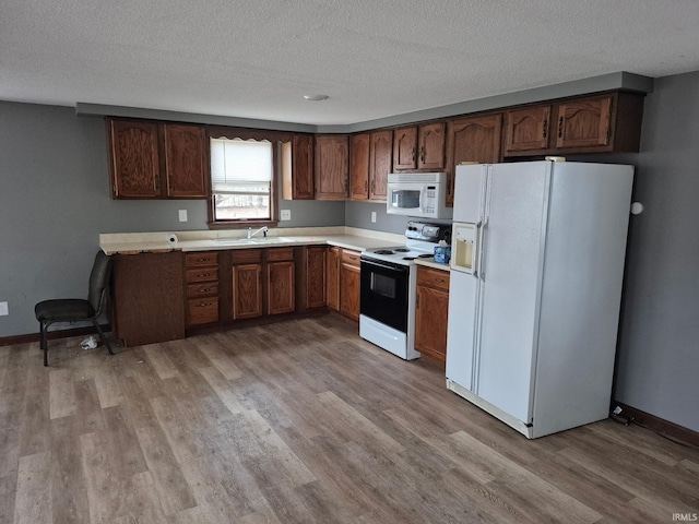 kitchen featuring light wood-type flooring, a textured ceiling, and white appliances